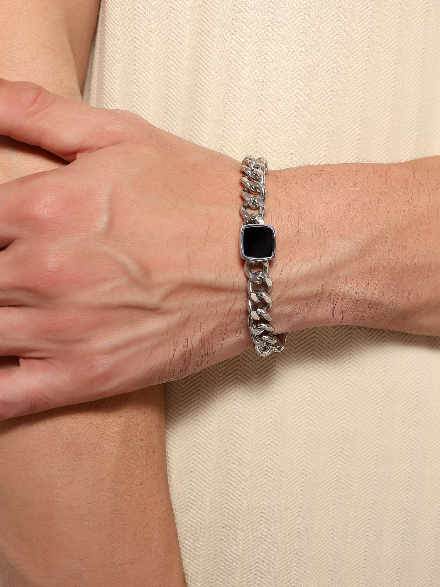 Side view of silver chain bracelet with black square accent on a man's wrist