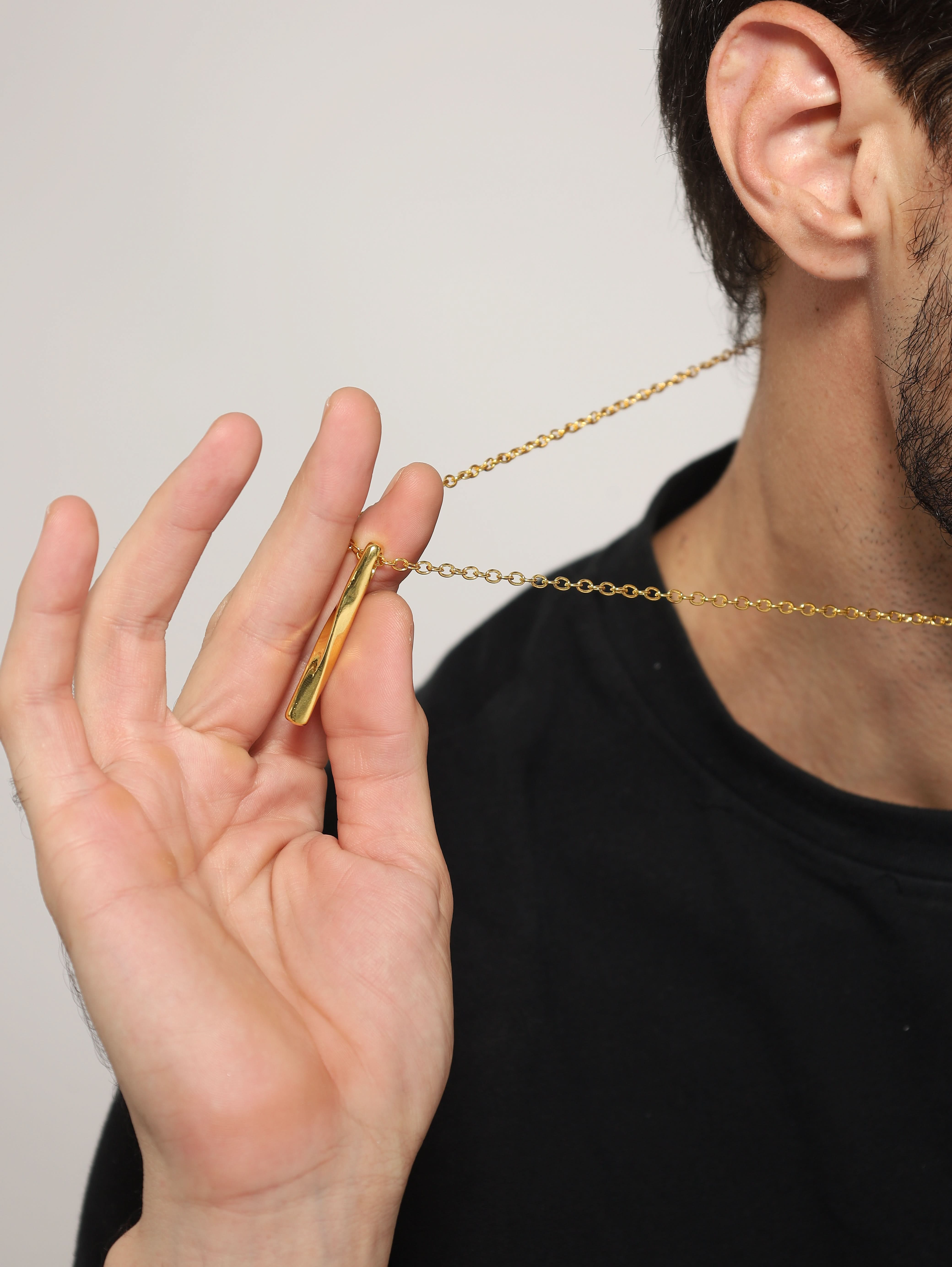 Model wearing Twisted Long Vertical Bar Pendant in gold — men's gold pendant styled on hand